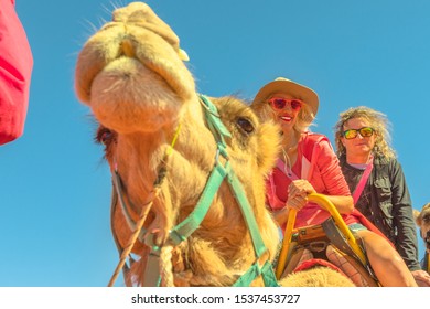 Couple Camel Riding In Australian Desert Of Northern Territory. Caucasian Tourists Enjoys Camel Ride On Red Dunes Of Red Centre, Central Australia. Popular Tourist Activity In Australian Outback.