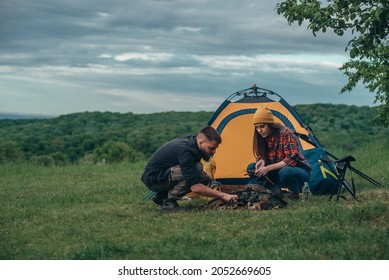 Couple Of Campers Lighting Up A Camp Fire Near The Tent While Camping In The Nature