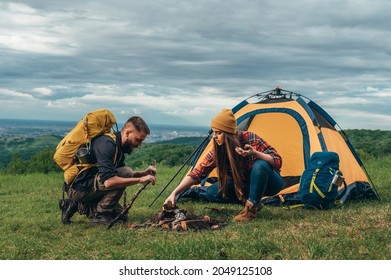 Couple of campers lighting a fire while setting up the camp tent during their time in the nature