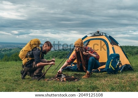 Couple of campers lighting a fire while setting up the camp tent during their time in the nature