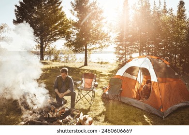 Couple, campfire and wood with smoke in nature by tent on grass field for outdoor vacation, holiday or weekend. Man preparing fire by woman for camping leisure, summer getaway or sunshine at forest - Powered by Shutterstock