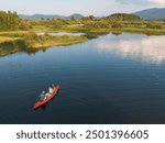 Couple canoeing on calm lake water at sunset enjoying the tranquility of surrounding green nature and colorful sky view.