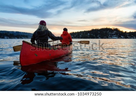 Couple canoeing on a wooden canoe in a beautiful Canadian Mountain Landscape during a vibrant winter sunset. Taken in Indian Arm, Vancouver, British Columbia, Canada.