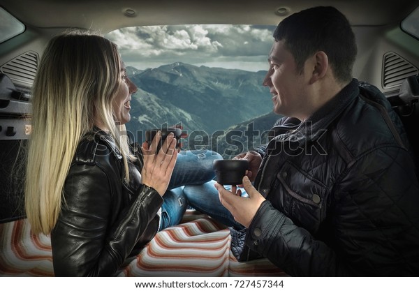 Couple in car. Blonde female and male drink\
tea in trunk in them car at autumn\
day.