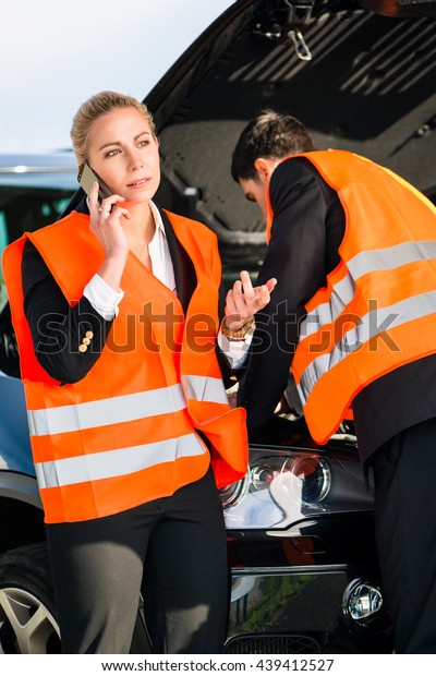 Couple with car breakdown wearing reflective\
vests calling towing\
company