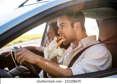 Couple In Car - Man Is Driving And Eating Baguette