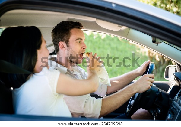 Couple\
in car - man is driving and woman is feeding\
him