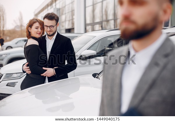 Couple in a car salon.\
Family buying the car. Elegant woman with her husband. Assistant\
with a clients