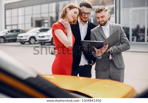 Couple in a car salon.\
Family buying the car. Elegant woman with her husband. Assistant\
with a clients