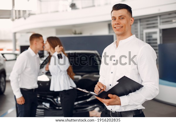 Couple in a car salon. Family buying the car.\
Handsome assistant with\
people