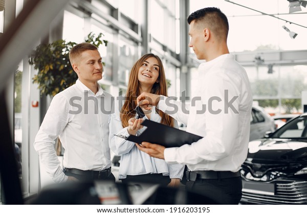 Couple in a car salon. Family buying the car.\
Handsome assistant with\
people