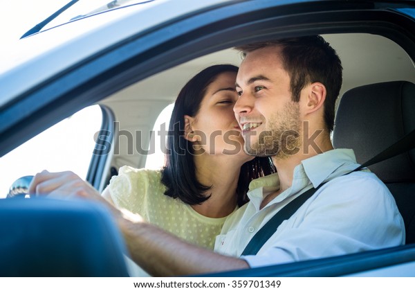 Couple in car - young woman kissing man in car\
while driving