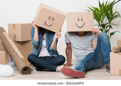 Couple With Cardboard Boxes On Their Heads With Smiley Face Sitting On Floor After The Moving House