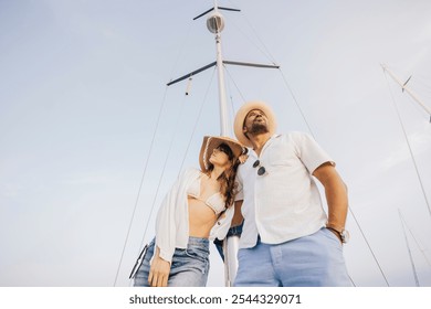 Couple in casual attire and sun hats, relaxing on a yacht under a clear blue sky, during their vacation. - Powered by Shutterstock