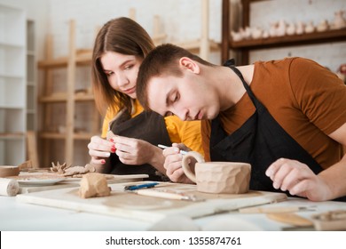 couple in casual clothes and aprons making ceramic pot on pottery at table in workshop - Powered by Shutterstock