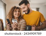 Couple caucasian man and woman husband and wife or boyfriend and girlfriend use mobile phone and credit card shopping online buy stuff or pay make payment booking e-commerce from home real people