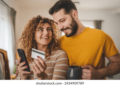 Couple caucasian man and woman husband and wife or boyfriend and girlfriend use mobile phone and credit card shopping online buy stuff or pay make payment booking e-commerce from home real people - Powered by Shutterstock