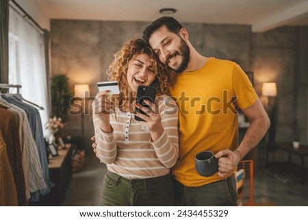 Couple caucasian man and woman husband and wife or boyfriend and girlfriend use mobile phone and credit card shopping online buy stuff or pay make payment booking e-commerce from home real people