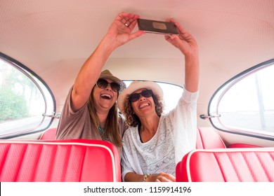 Couple Of Caucasian Middle Age Woman In Outdoor Leisure Activity Near And Sitting On A Red Vintage Car Ready To Travel.