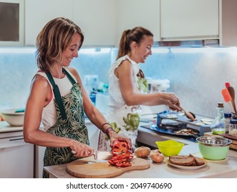 A Couple Of Caucasian Women Cook And Have Fun Together. In The Kitchen. One Of Them Slices A Bell Pepper. Family And Diversity Concept. Lgbt.