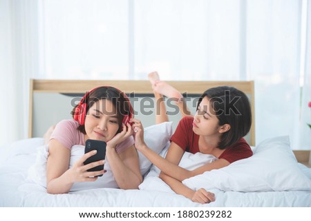 Couple caucasian women teasing to pull a headphones on the bed in the morning