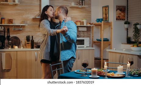 Couple celebrating by dancing sitting in the kitchen, during festive dinner. Happy in love couple dining together at home, enjoying the meal, smiling, having fun, celebrating their anniversary. - Shutterstock ID 1837632019
