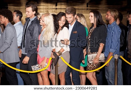 Couple with cell phone standing in queue outside nightclub