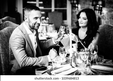 Couple with champange glasses dating and toasting in restaurant in black and white