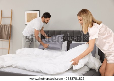 Couple changing bed linens in room. Domestic chores
