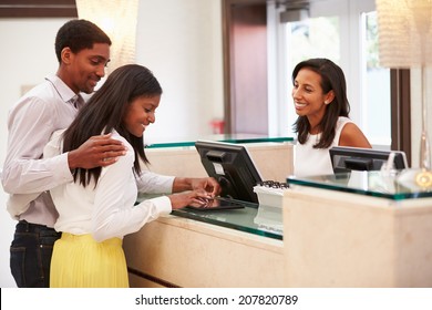 Couple Checking In At Hotel Reception Using Digital Tablet