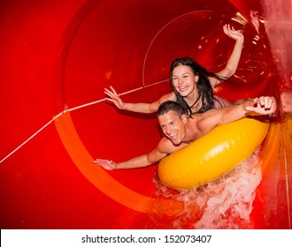 Couple cheering while having fun sliding down a water slide at public swimming pool