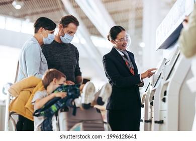 Couple With Child 0n Luggage Trolley Taking Help Of Airlines Staff At Self Service Machine At Airport. Airport Attendant Helping Tourist Family With Self Check-in At Airport During Pandemic.