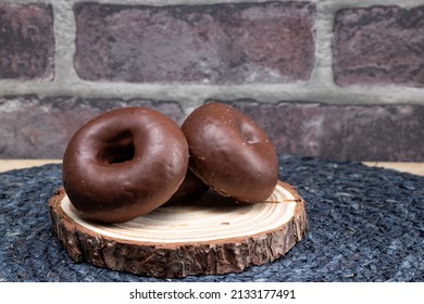 A couple of chocolate-covered donuts on a wood plate