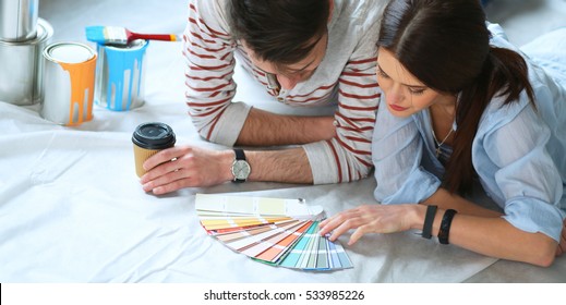 Couple Choosing Paint Colour From Swatch For New Home Lying On Wooden Floor