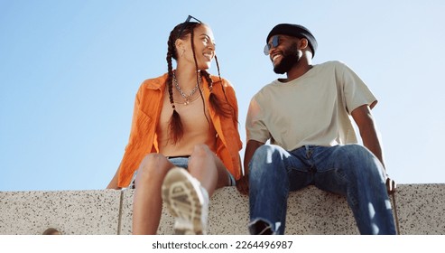 Couple, city and relax with a black man and woman sitting on a wall outdoor against a clear blue sky together. Street style, travel and love with a happy male and female bonding outside during summer