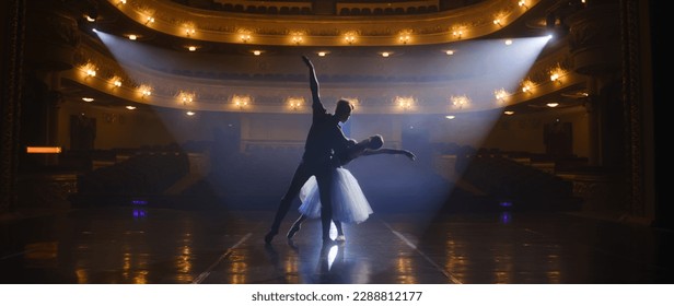 Couple of classical ballet dancers practice on theatre stage before performance. Man in training suit lifts graceful ballerina. Dance choreography rehearsal. Illuminated theatrical hall. Slow motion. - Powered by Shutterstock