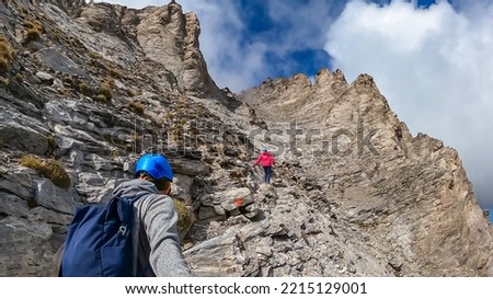 Couple climbing on mystical foggy hiking trail leading to Mount Olympus (Mytikas, Skala, Stefani) in Mt Olympus National Park, Thessaly, Greece, Europe. Scenic view of cloud covered slopes and ridges