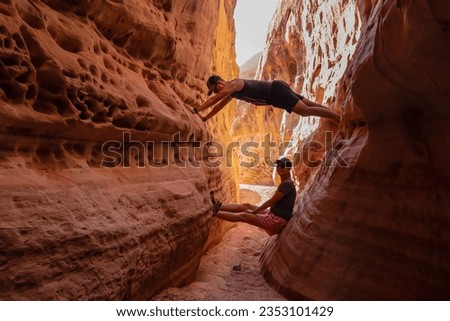 Couple climbing the walls in narrow Kaolin Wash slot canyon on White Domes Hiking Trail in Valley of Fire State Park in Mojave desert, Nevada, USA. Massive cliffs of striated red white rock formations