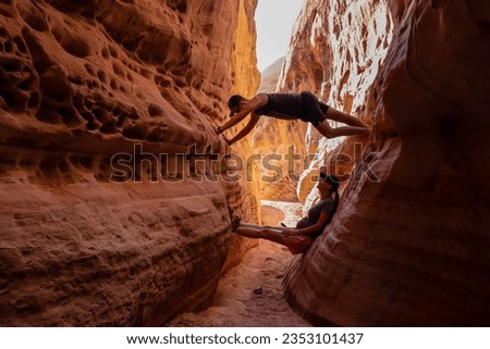 Couple climbing the walls in narrow Kaolin Wash slot canyon on White Domes Hiking Trail in Valley of Fire State Park in Mojave desert, Nevada, USA. Massive cliffs of striated red white rock formations
