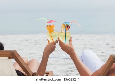 Couple clinking glasses of cocktail on beach in front of ocean