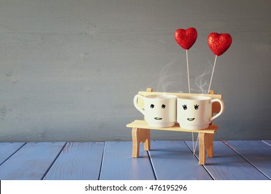 Couple coffee cups on old bench next to red glitter hearts. vintage filtered. Romance and weekend concept
