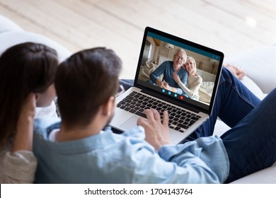 Couple communicating with elderly parents living abroad using computer and videocall application, laptop screen view over spouse shoulder. Distant virtual communication modern technology usage concept - Shutterstock ID 1704143764