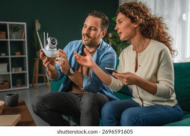 Couple configuring an security cctv camera for home security, connecting it to a mobile phone, and reviewing smart home surveillance technology settings together in a modern interior