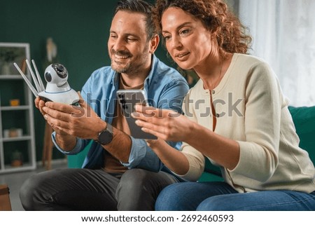 Couple configuring an security cctv camera for home security, connecting it to a mobile phone, and reviewing smart home surveillance technology settings together in a modern interior