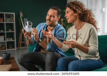 Couple configuring an security cctv camera for home security, connecting it to a mobile phone, and reviewing smart home surveillance technology settings together in a modern interior