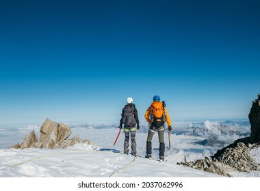 Couple Connected Team Rope  With Climbing Harness Dressed Mountaineering Clothes With Backpacks And Ice Axes Enjoying Views Ascending Mont Blanc (Monte Bianco) Summit Near Aiguille Du Midi, France.