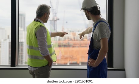 Couple Of Construction Workers On Workplace, Young Electrician Technician And Contractor Foreman Talking Together On Building Site, Engineer And Architect Meeting For Project Working