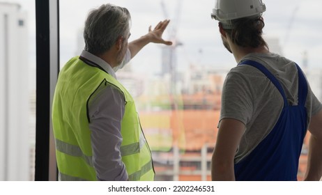 Couple Of Construction Workers On Workplace, Young Electrician Technician And Contractor Foreman Talking Together On Building Site, Engineer And Architect Meeting For Project Working