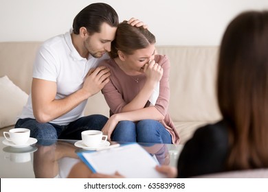 Couple counseling. Upset crying young woman having emotional breakdown, wiping tears, loving boyfriend trying to comfort girlfriend embracing her, husband consoling depressed wife at the psychologist