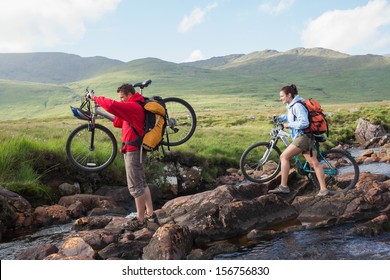 Couple crossing a stream holding their bikes in the mountains - Powered by Shutterstock